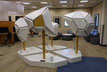 A sculpture with four separate pieces. All are white, padded shapes. The sculpture is in a computer room.